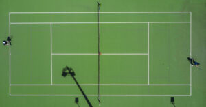 Aerial view of a standard-sized pickleball court with marked white boundary lines on a green surface, showing the net at center