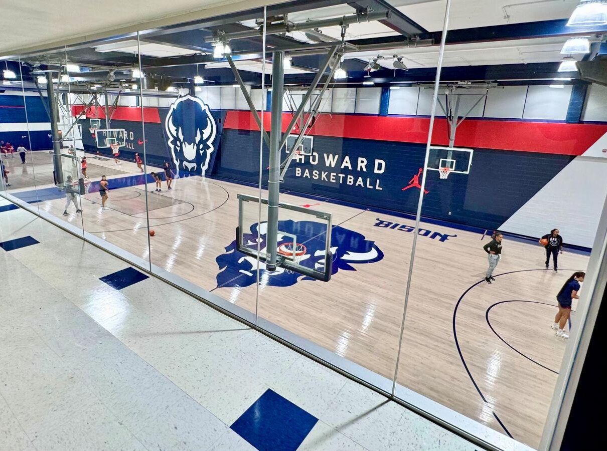 Completed hardwood gymnasium floor renovation at Howard University featuring navy blue and red court markings, Howard Bison logos, and custom HU center court design