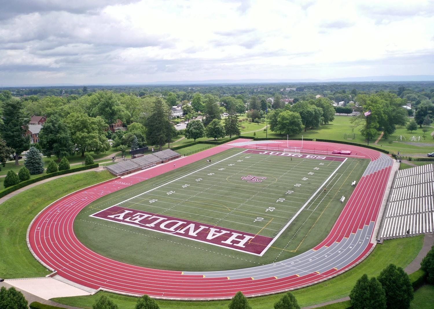 Completed outdoor track and field installation at John Handley High School in Winchester Virginia featuring crimson red running surface, multi-lane competition track, and green artificial turf football field