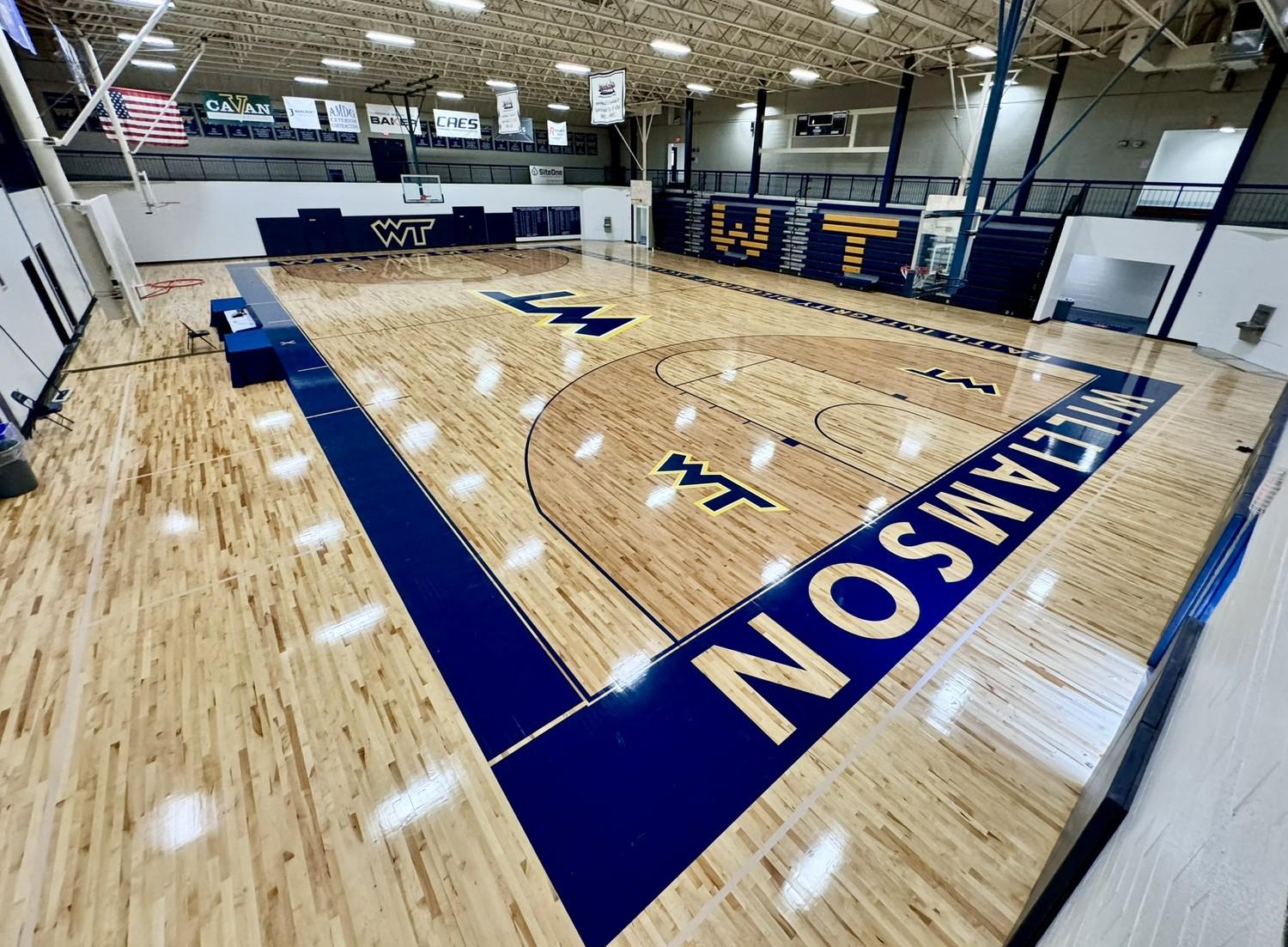 Completed hardwood gymnasium floor renovation at Williamson College of the Trades featuring navy blue court markings and WT logos