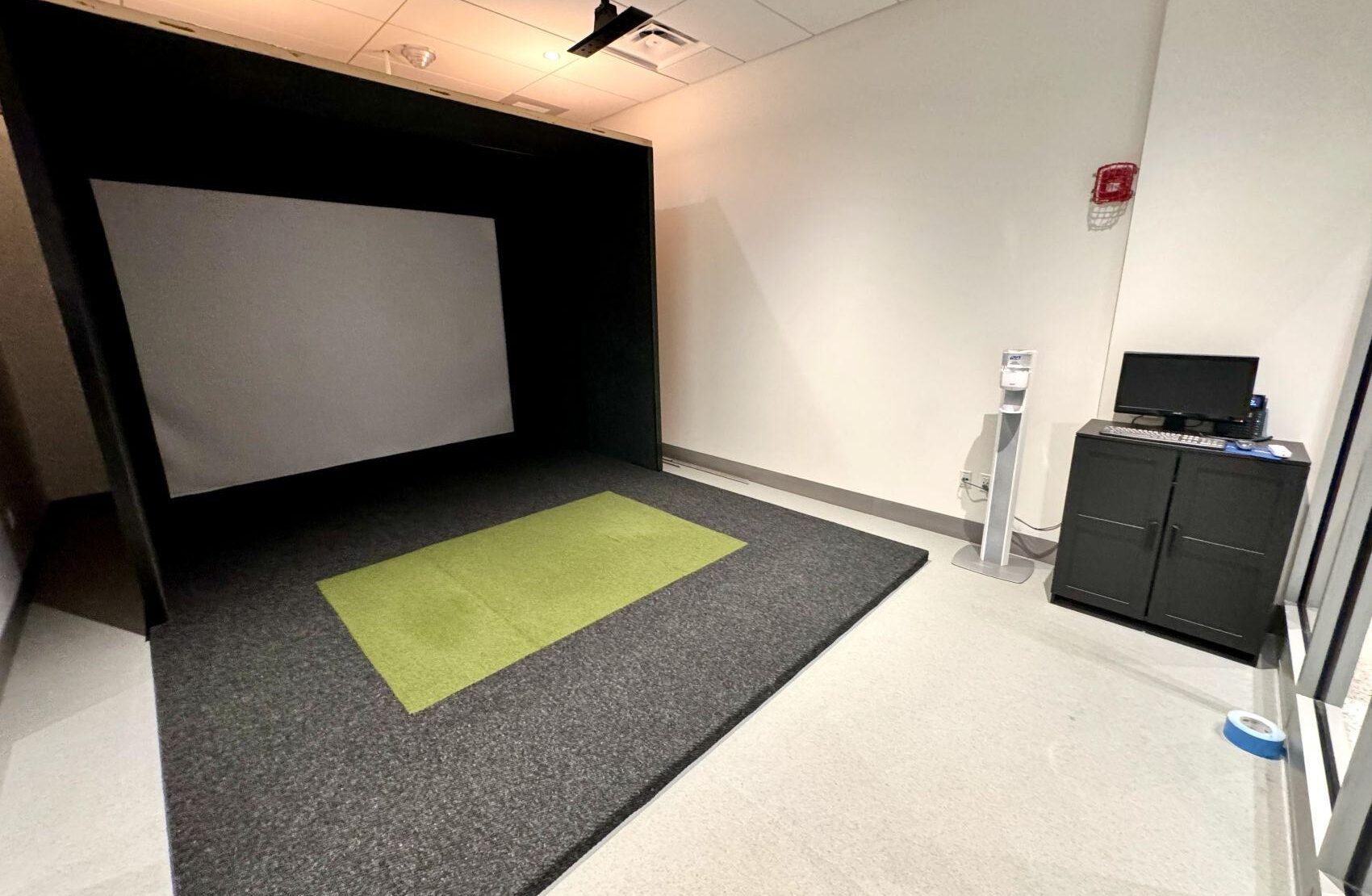 Indoor golf simulator room with projection screen, hitting mat, and launch monitor