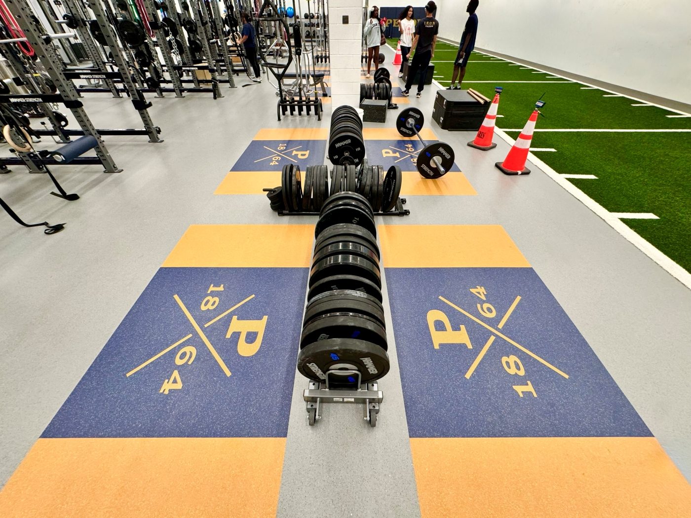 Indoor turf sprint lane alongside Hammer Strength power racks and branded lifting platforms at Peddie School Athletic Center