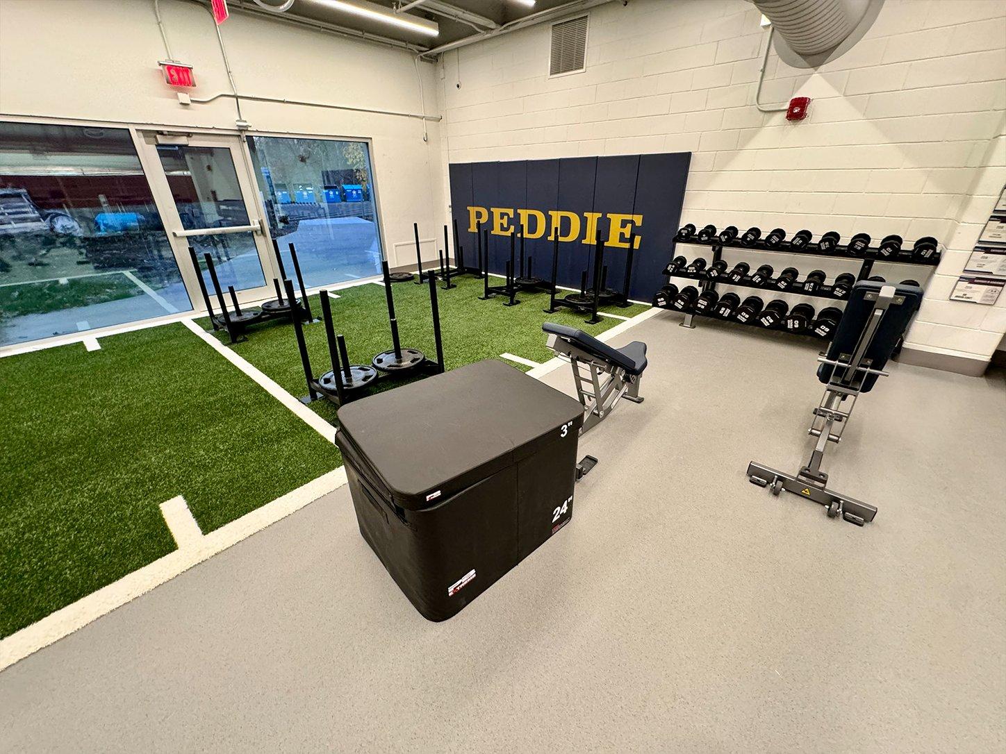Wide view of Peddie School Athletic Center performance weight room with Hammer Strength power racks and custom navy and gold flooring