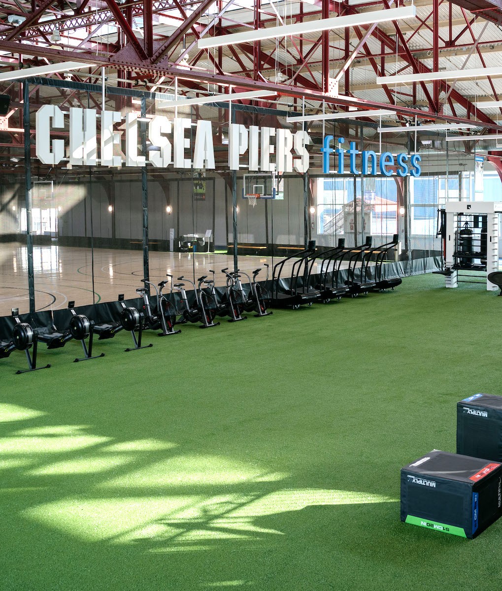 Chelsea Piers NYC turf training area with rowing machines, air bikes, and treadmills alongside a basketball court
