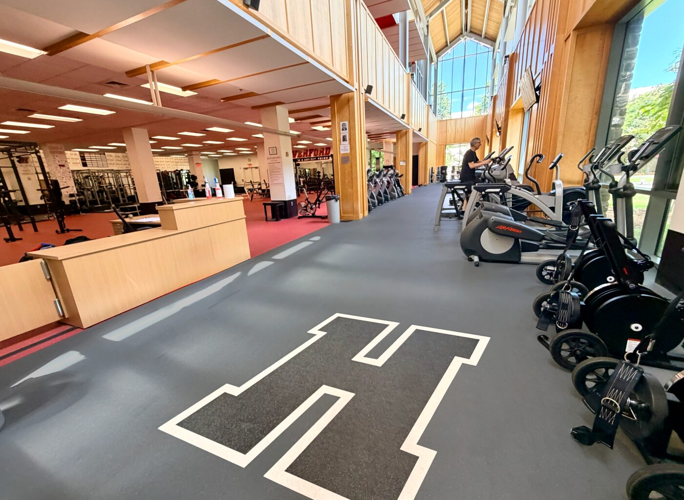 Haverford College fitness center showing gray Mondo Valor S flooring transitioning to a red cardio zone with spin bikes and treadmills under a wood-paneled atrium.
