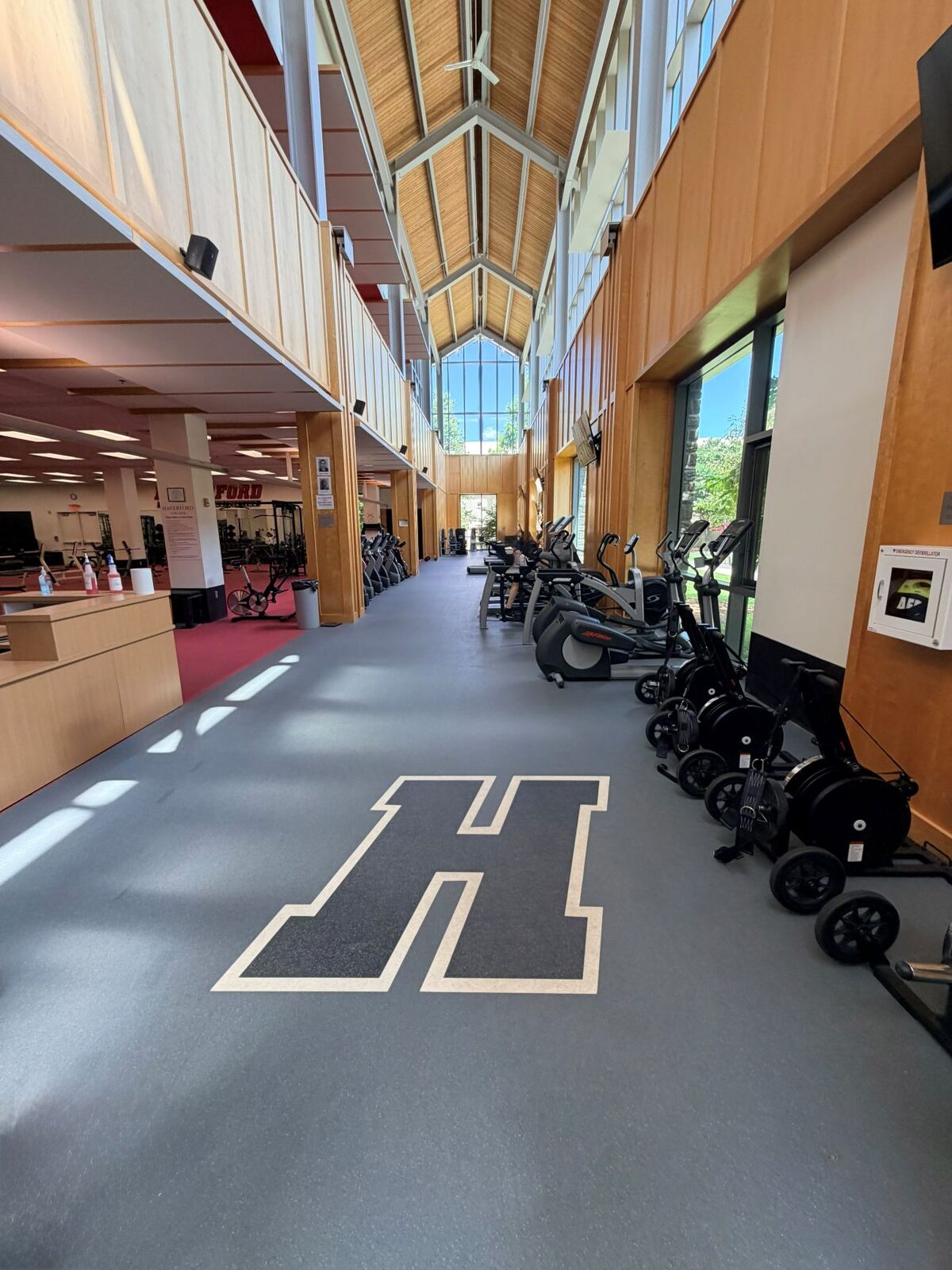 Close-up of red textured power lifting mats meeting gray Mondo Valor S rubber flooring in the Haverford College weight room, with a treadmill by the window.