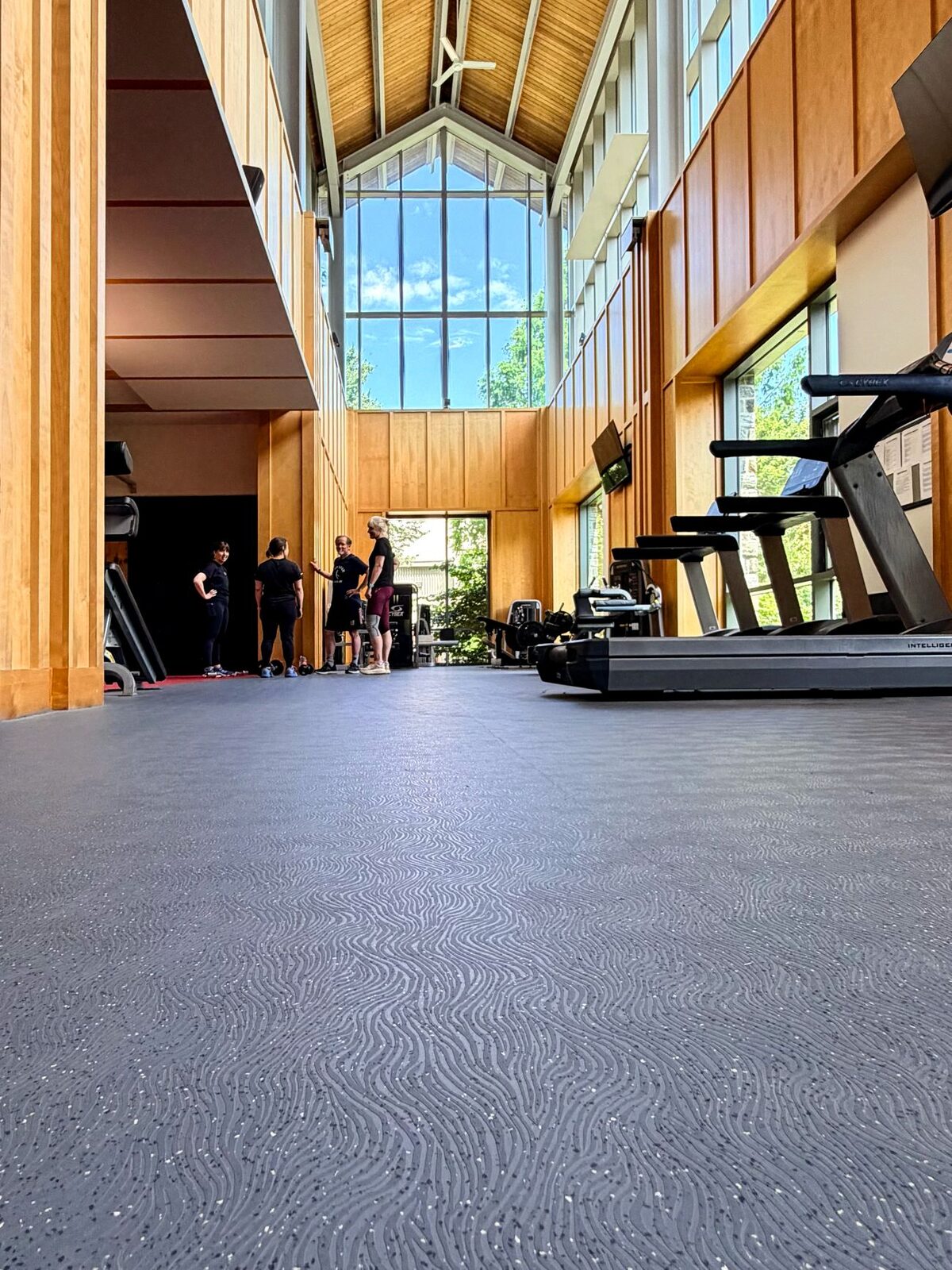 Vertical view of the Haverford College weight room with the water-jet cut H logo on gray Mondo Valor S flooring, a row of cardio machines along the wall.