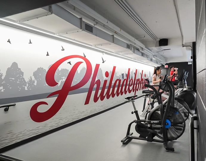 O'Pake Recreation Center cardio room with air bikes and a custom Philadelphia skyline wall mural