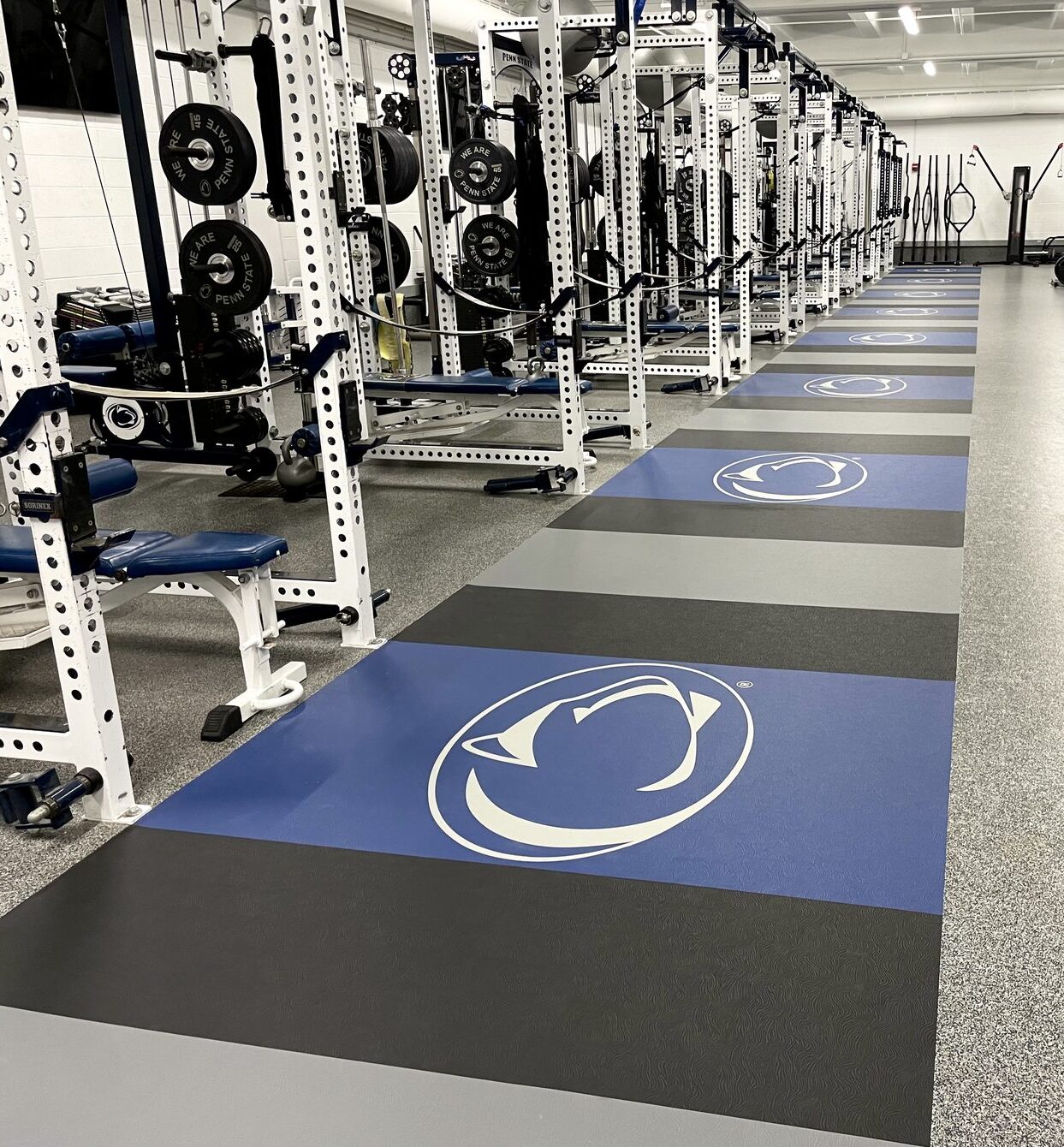 Penn State Rec Hall weight room with white strength racks and Nittany Lion logo flooring inlays