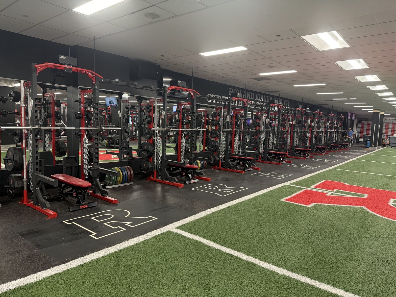 Row of strength racks with chains at Rutgers' Garutti Strength and Conditioning Center, opening directly onto the football practice field