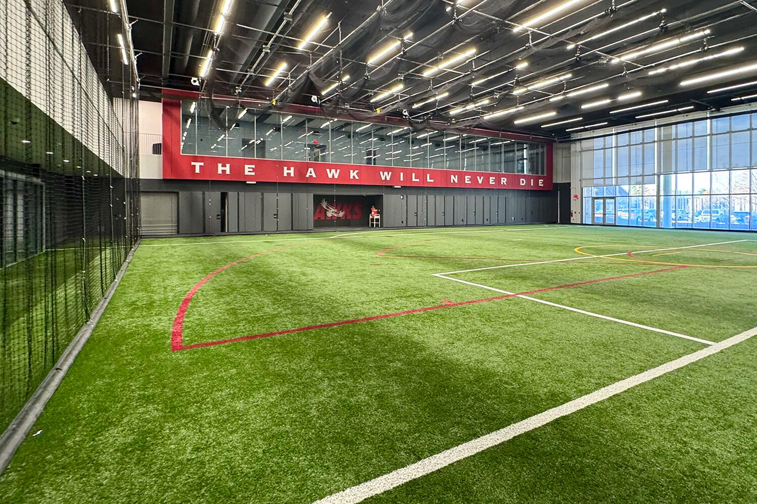 Wide view of St. Joseph's University's indoor turf training field with batting cage netting and Hawks branding